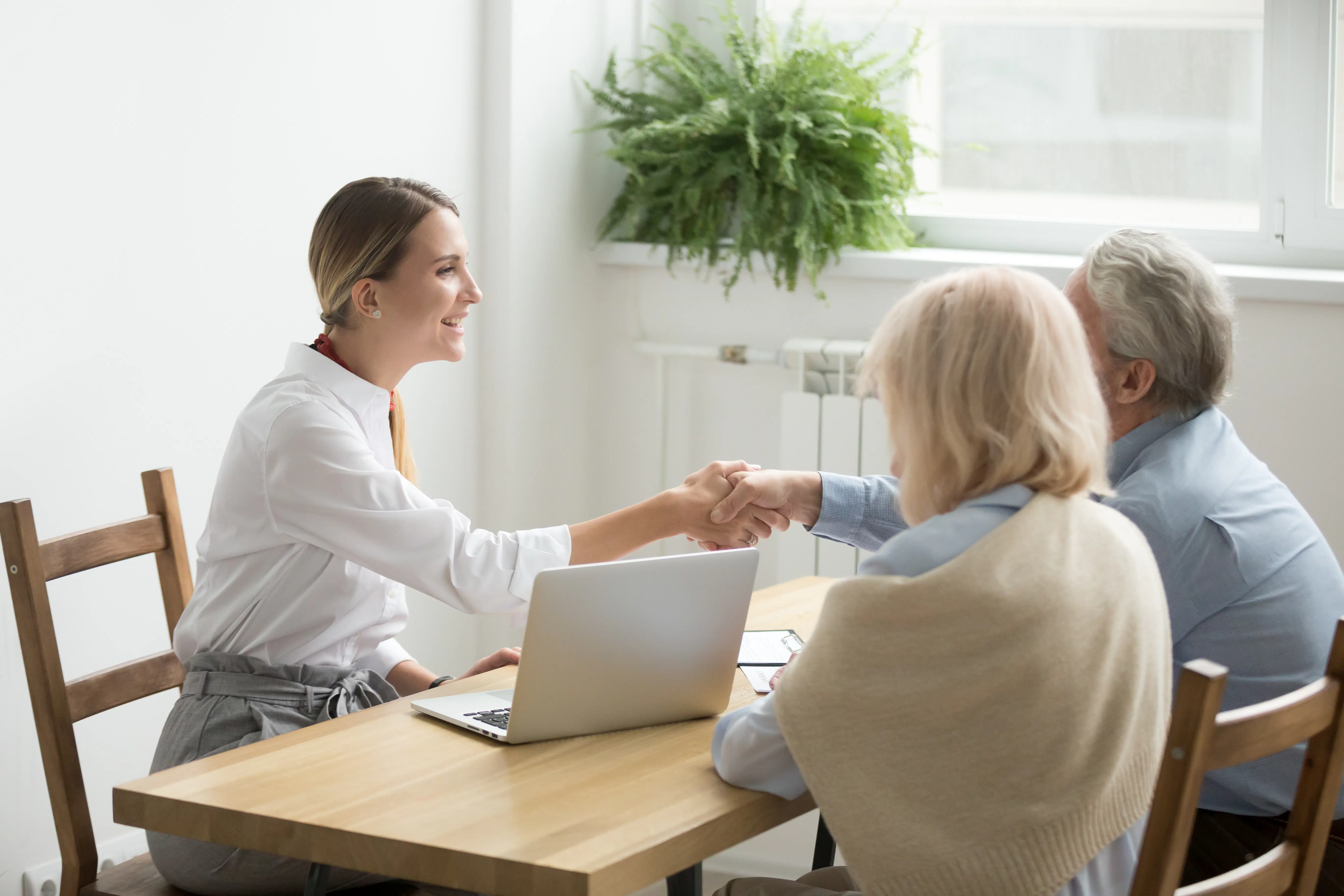 Smiling female lawyer shakes hand with senior couple.
