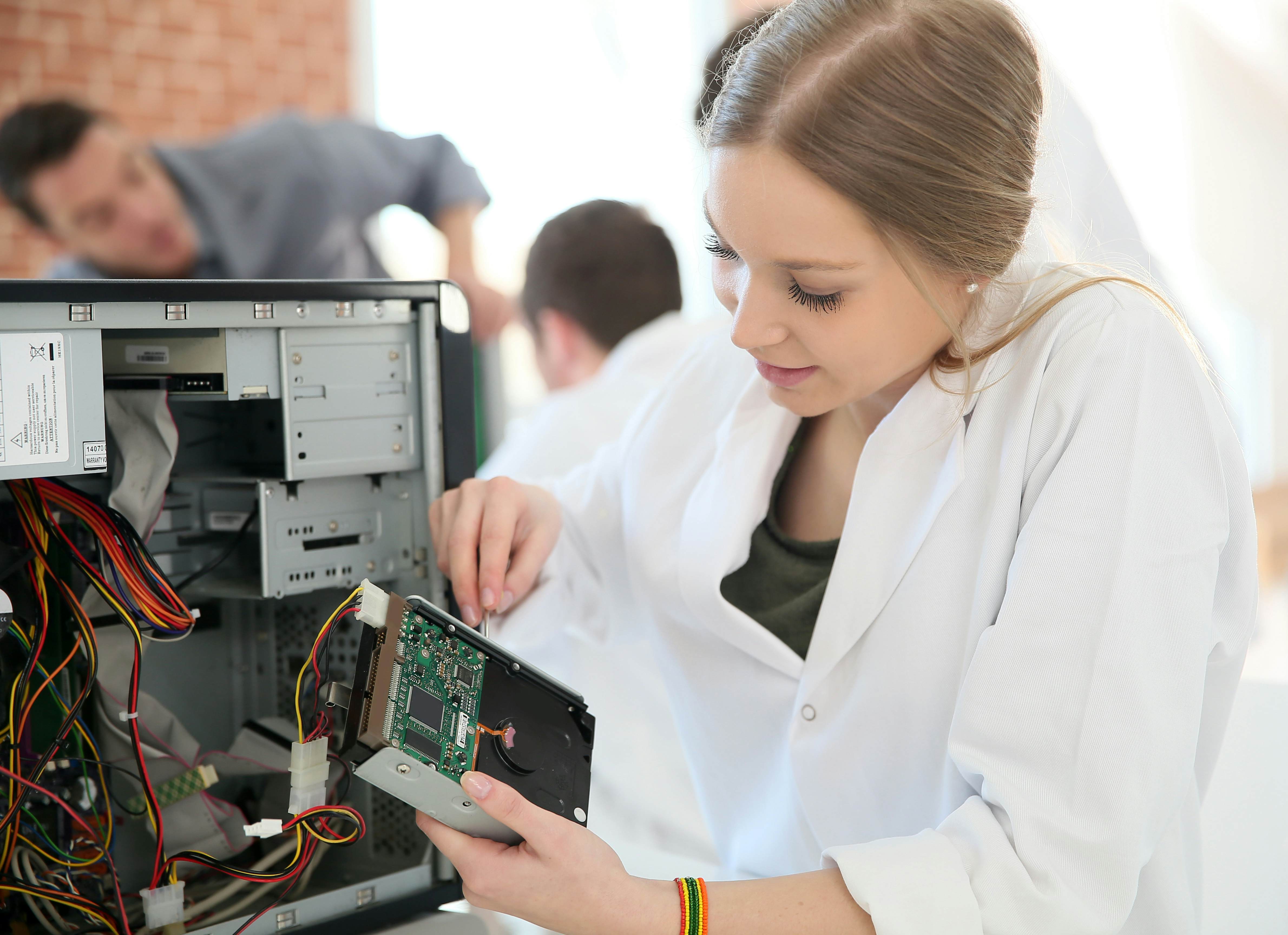 Young female Computer Science student removes the hard drive from a computer case