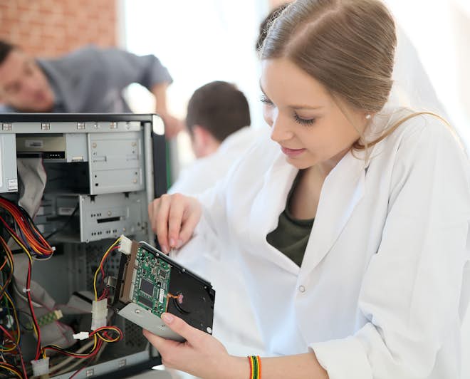 Young female Computer Science student removes the hard drive from a computer case